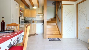A kitchen with wooden beams, a dining area with a table set for two, and a staircase leading to another level. - Quiet house with garden and parking near Lessay (Laulne)