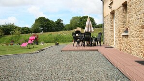 A patio area with outdoor seating, a stone wall, and a grassy field in the background. - Quiet house with garden and parking near Lessay (Laulne)