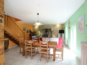 Zona pranzo con tavolo e sedie in legno, camino in pietra e una scala che conduce a un piano superiore.