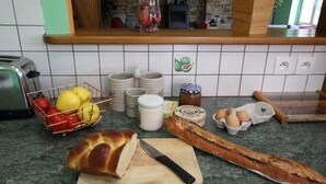 A kitchen counter with a loaf of bread, a baguette, a basket of apples, and a jar of jam.