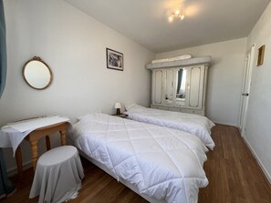 Une chambre avec deux lits, une chaise en bois, une petite table, un miroir et une armoire.