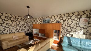 Een woonkamer met een beige bank, een blauwe bank, een houten kast en een televisie.