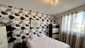 Een slaapkamer met een bed, nachtkastje, kledingkast, bureau en een raam met gordijnen.