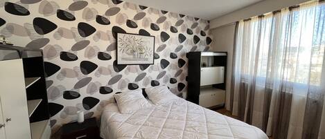 A bedroom with a bed, a nightstand, a wardrobe, a desk, and a window with curtains.