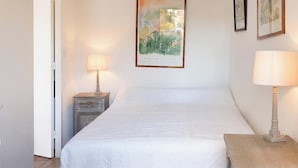 A bedroom with a bed, a nightstand with a lamp, a wall-mounted painting, and a door.