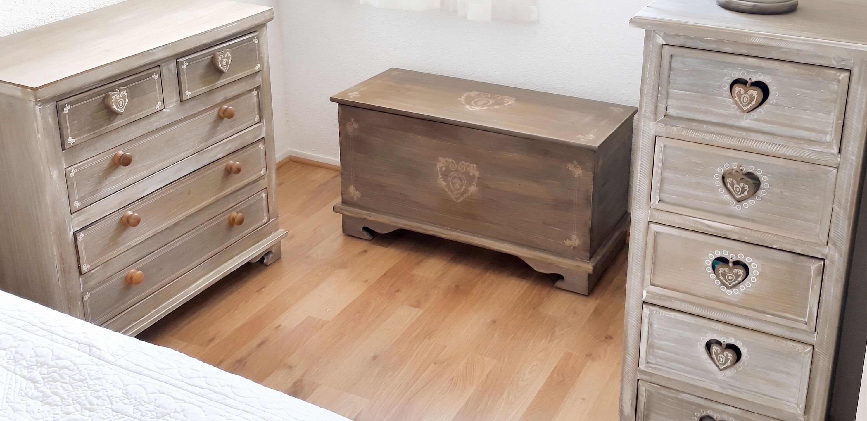 Un dormitorio con cama, dos cómodas de madera con tiradores con forma de corazón y un pequeño aparador.