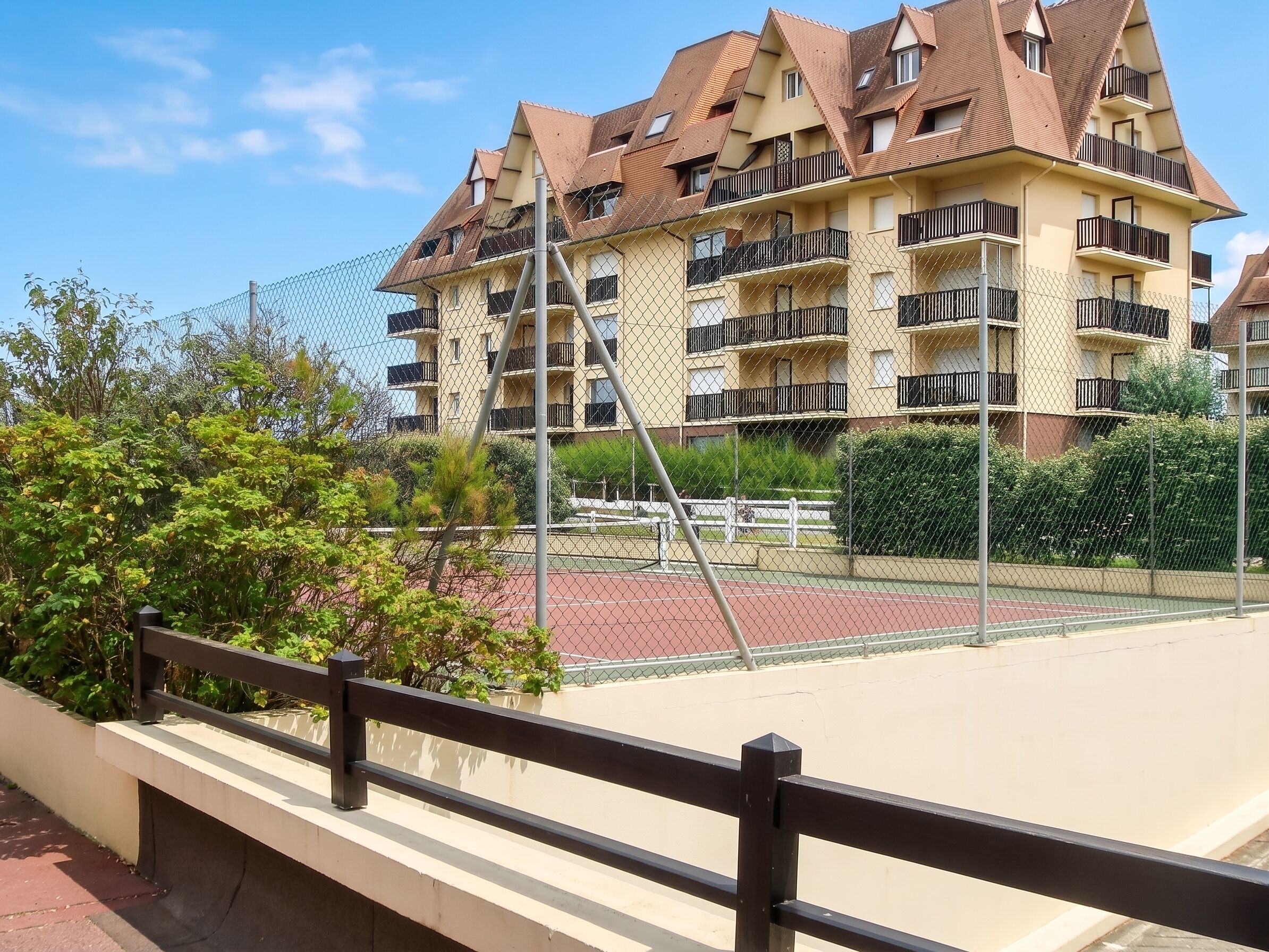 A multi-story residential building with balconies, a tennis court, and a chain-link fence.
