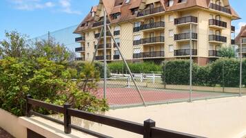 A multi-story residential building with balconies, a tennis court, and a chain-link fence.