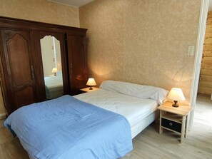 Une chambre à coucher avec un lit, deux tables de chevet avec des lampes, une armoire en bois et un miroir.
