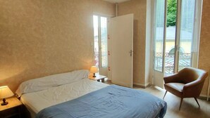 A bedroom with a bed, a chair, a nightstand, and a window with a view of greenery. - 2-room apartment, 4 beds in Cauterets near thermal baths (Cauterets)