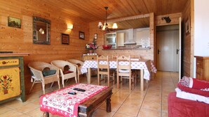 Interior acogedor de una cabaña de madera con comedor, pequeña cocina y sala de estar con sofá rojo.