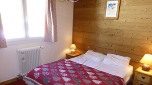 Un dormitorio acogedor con cabecera de madera, colcha estampada roja, dos lámparas de noche y un cuadro en la pared.