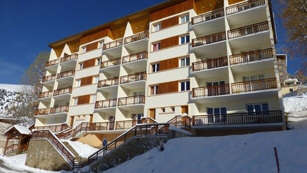 Un hotel de varios pisos con balcones, un telesilla y un paisaje nevado.