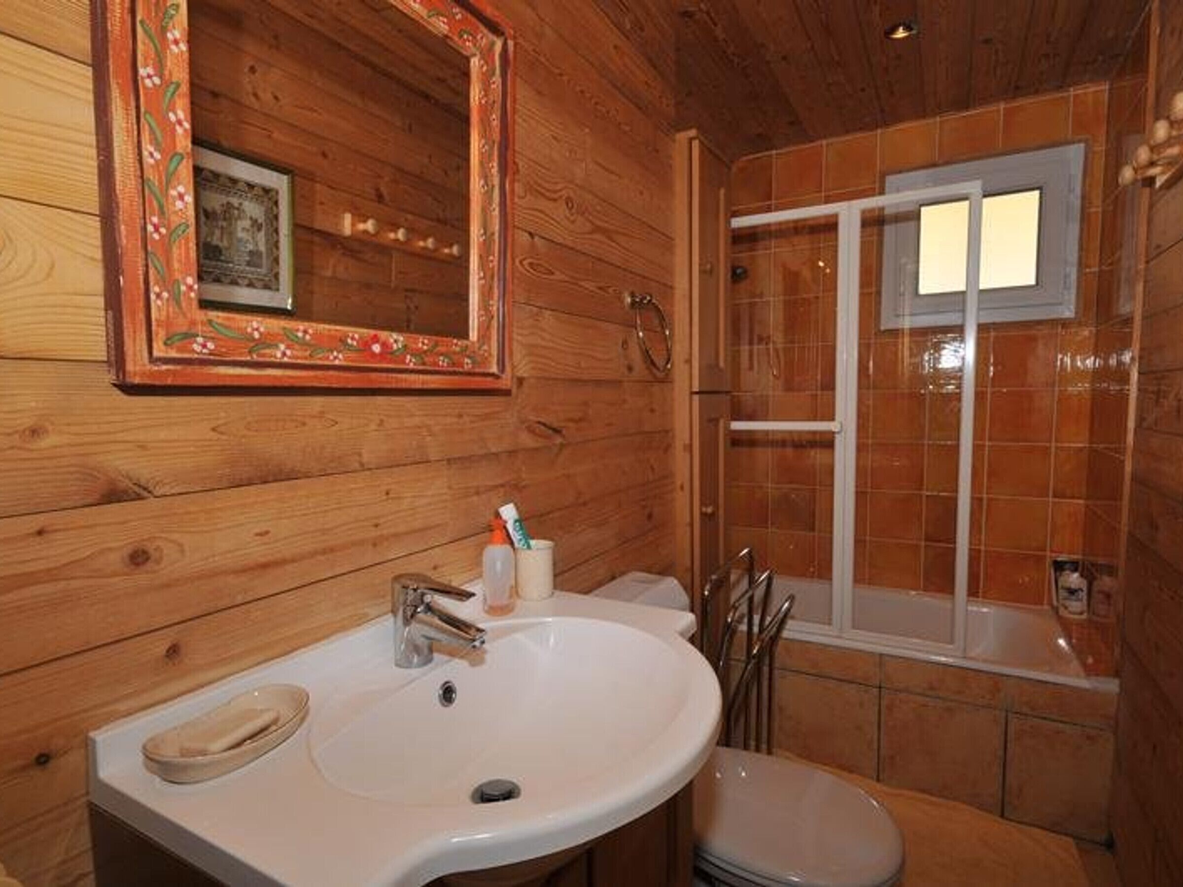 A wooden bathroom with a sink, mirror, and shower.