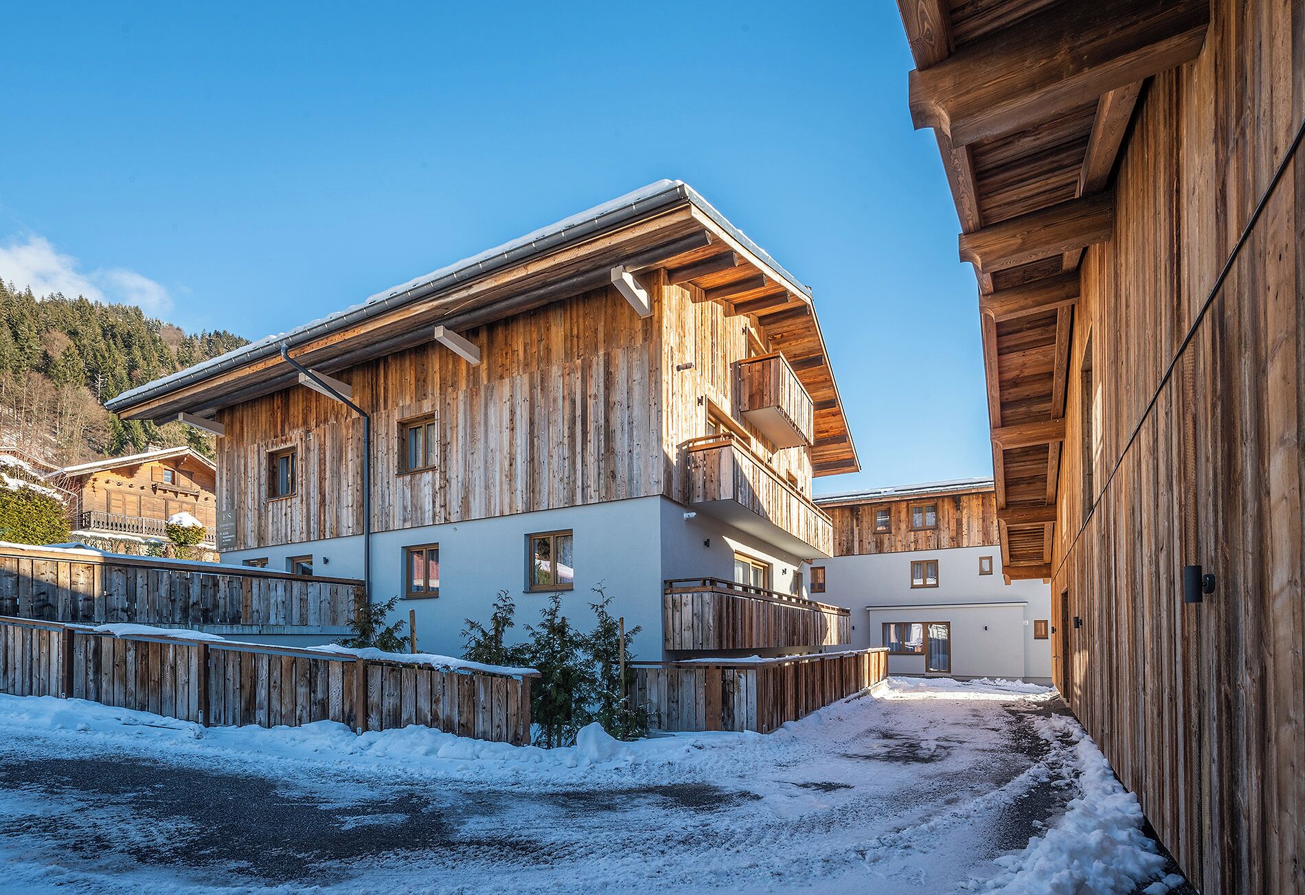 Un chalet en bois doté de balcons, un sol recouvert de neige et un paysage montagneux en toile de fond.