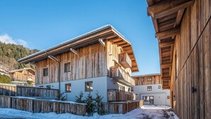 Un chalet en bois doté de balcons, un sol recouvert de neige et un paysage montagneux en toile de fond.