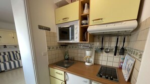Ett kompakt kök med mikrovågsugn, kaffebryggare och en gasspis. Det finns skåp och en diskho.