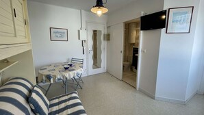 Ett kompakt bostadsutrymme med en matplats, en soffa, en tv och en dörr som leder till ett badrum.