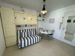 A compact room with a striped sofa, a small dining table, and a cabinet with shelves.