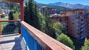 Ein Holzbalkon mit blauer Reling mit Blick auf eine gebirgige Landschaft und mehrere mehrstöckige Gebäude.