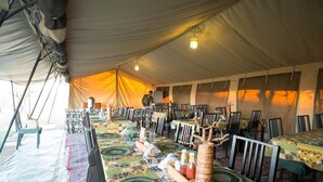 A tented dining area with tables covered in patterned tablecloths, chairs, and a central decorative tree. - Serengeti Wildebeest Camp (Serengeti)