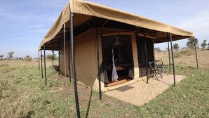 A safari tent with a single entrance, a small table, and a chair outside. - Serengeti Wildebeest Camp (Serengeti)