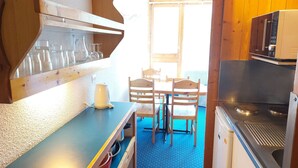 Una cucina compatta con zona pranzo, caratterizzata da un piano di lavoro blu, sedie di legno e un forno a microonde.