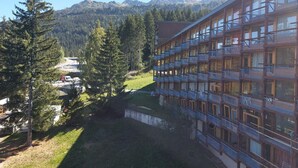 Un hotel a più piani con balconi, immerso tra alberi e montagne.