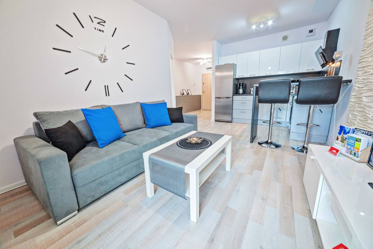 A modern living room with a grey sofa, a white coffee table, and a large wall clock.