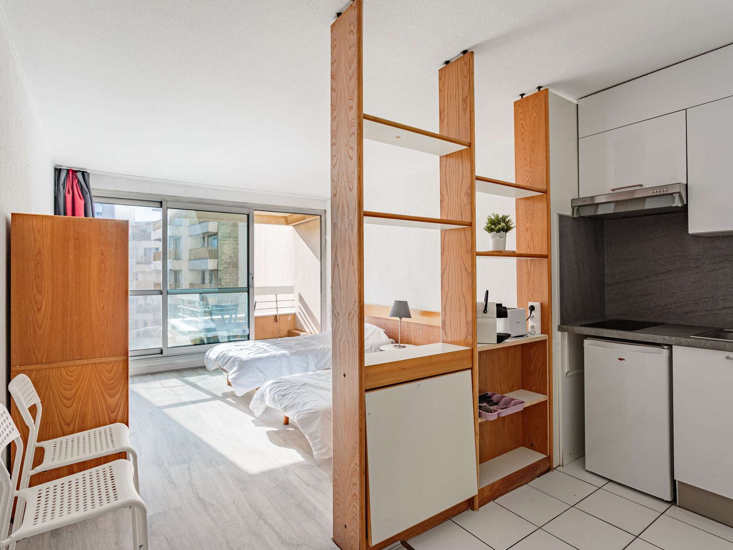 Une pièce compacte comprenant un lit, un bureau, une chaise, un coin cuisine et une porte coulissante donnant sur un balcon.