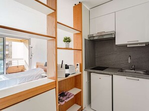 Eine kompakte Küche mit eingebautem Herd, einer Spüle und einem kleinen Kühlschrank. Es ist ein Holzregal mit einem Topfpflanzen darauf.