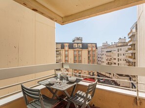 A balcony with a table set for dining, overlooking a cityscape with multi-story buildings.