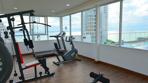 A gym with exercise equipment and large windows overlooking a body of water. - Serenity Wongamat Pattaya Studio (Pattaya)