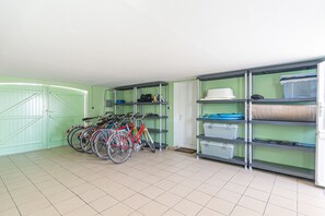 A room with a green door, tiled floor, and a bike rack with several bicycles. There are shelves with storage bins and a white door in the background. - Homerez - House in Bangor (Bangor)