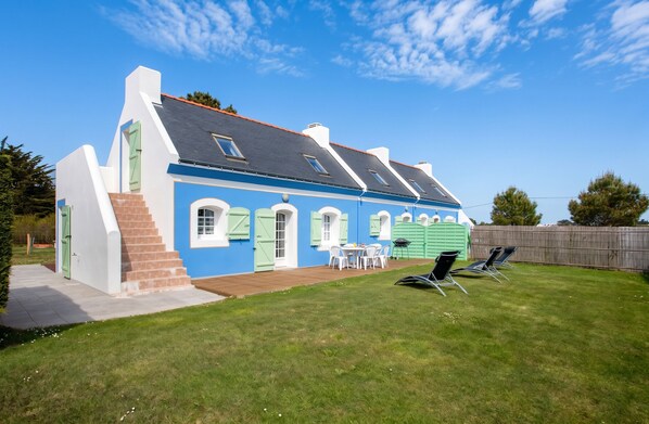 A two-story house with a blue exterior and white trim, a front porch with a table and chairs, and a fenced backyard with lawn chairs. - Homerez - House in Bangor (Bangor)