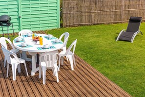 Ein runder Tisch mit weißen Stühlen, einem Grill und einer Holzterrasse.