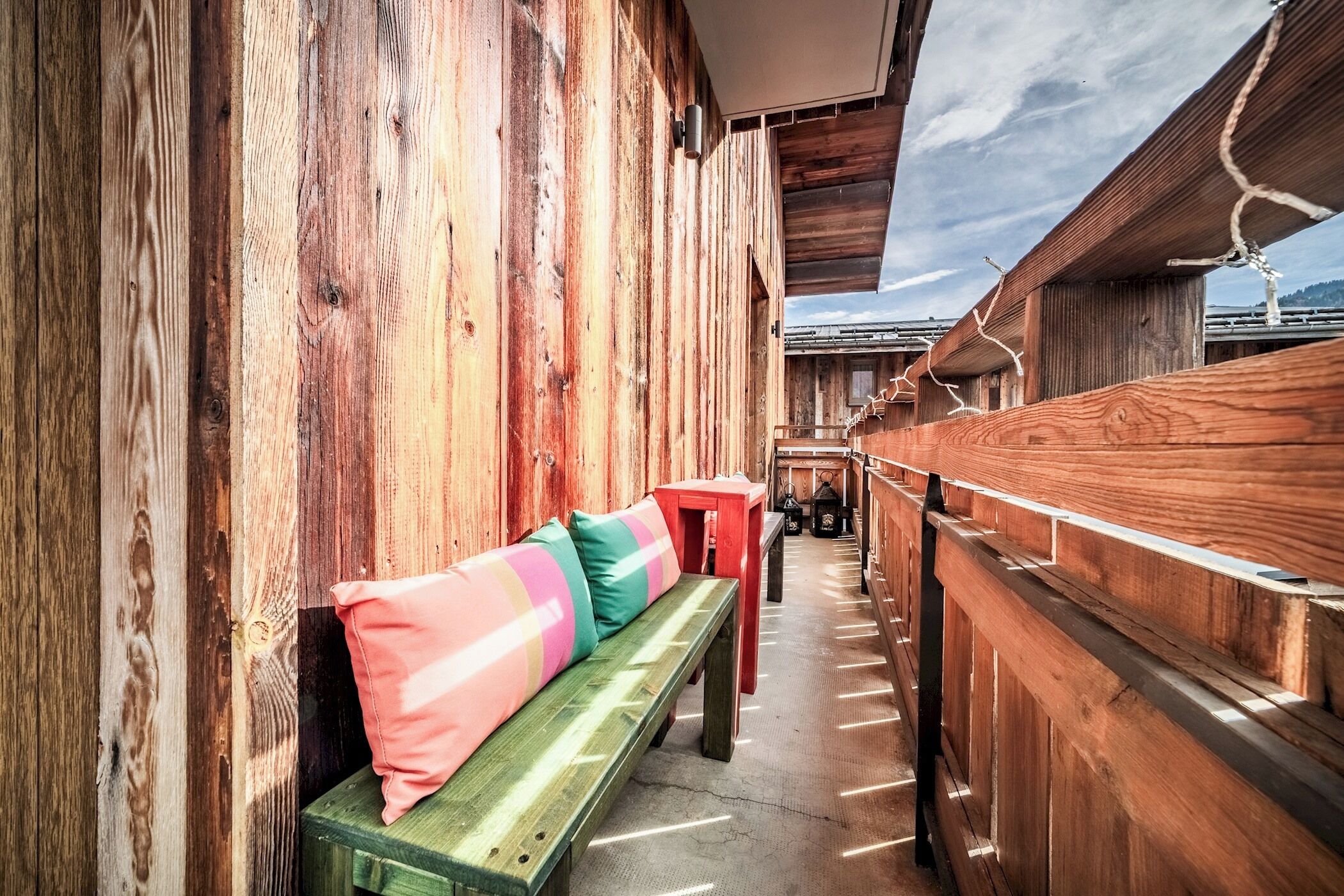 Un banc en bois agrémenté de coussins colorés, une table rouge et une rambarde en bois dans un intérieur rustique.