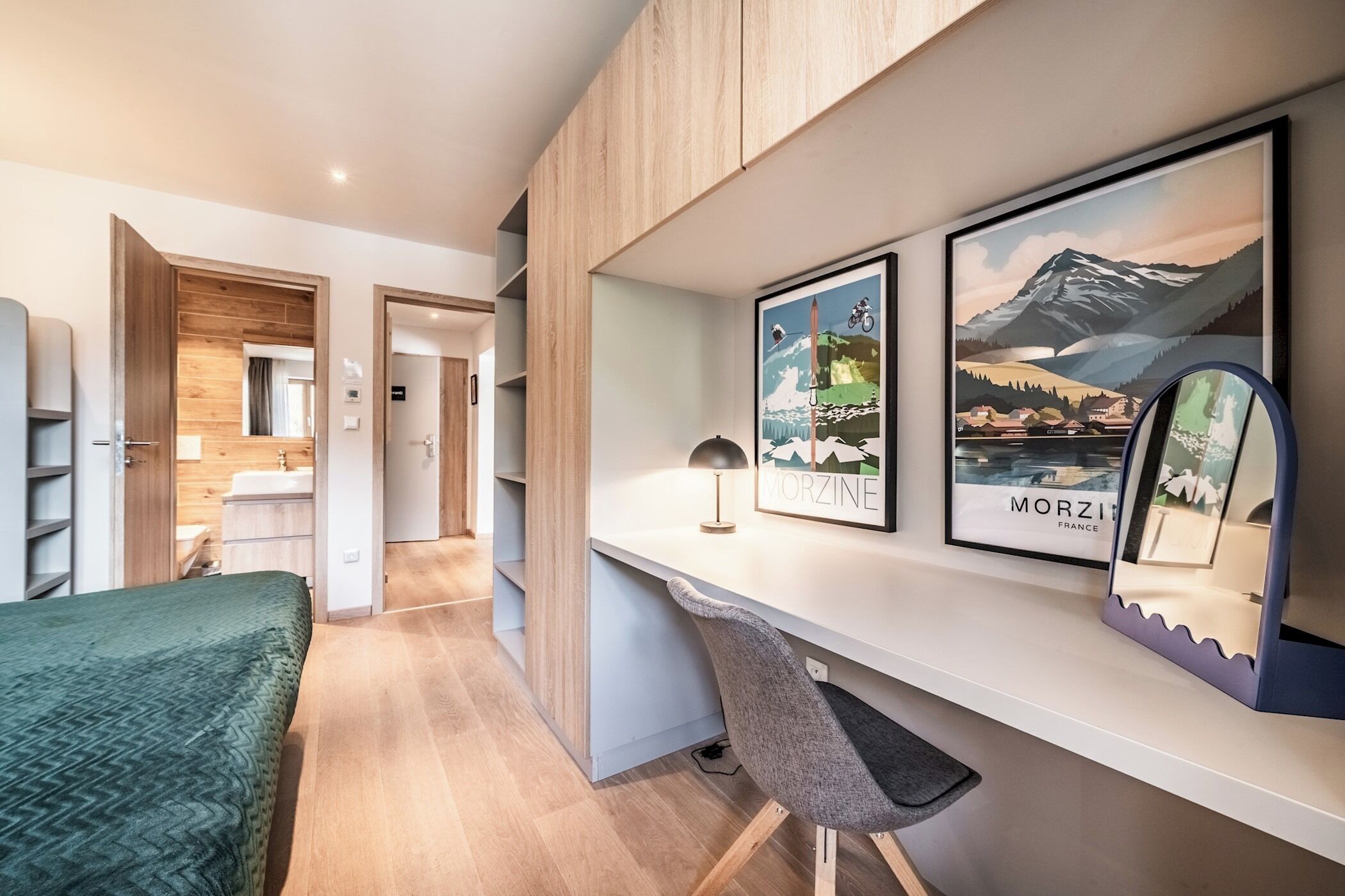 Ein modernes Hotelzimmer mit einem Bett, einem Schreibtisch und einem Stuhl. An den Wänden befinden sich gerahmte Bilder und ein Spiegel.