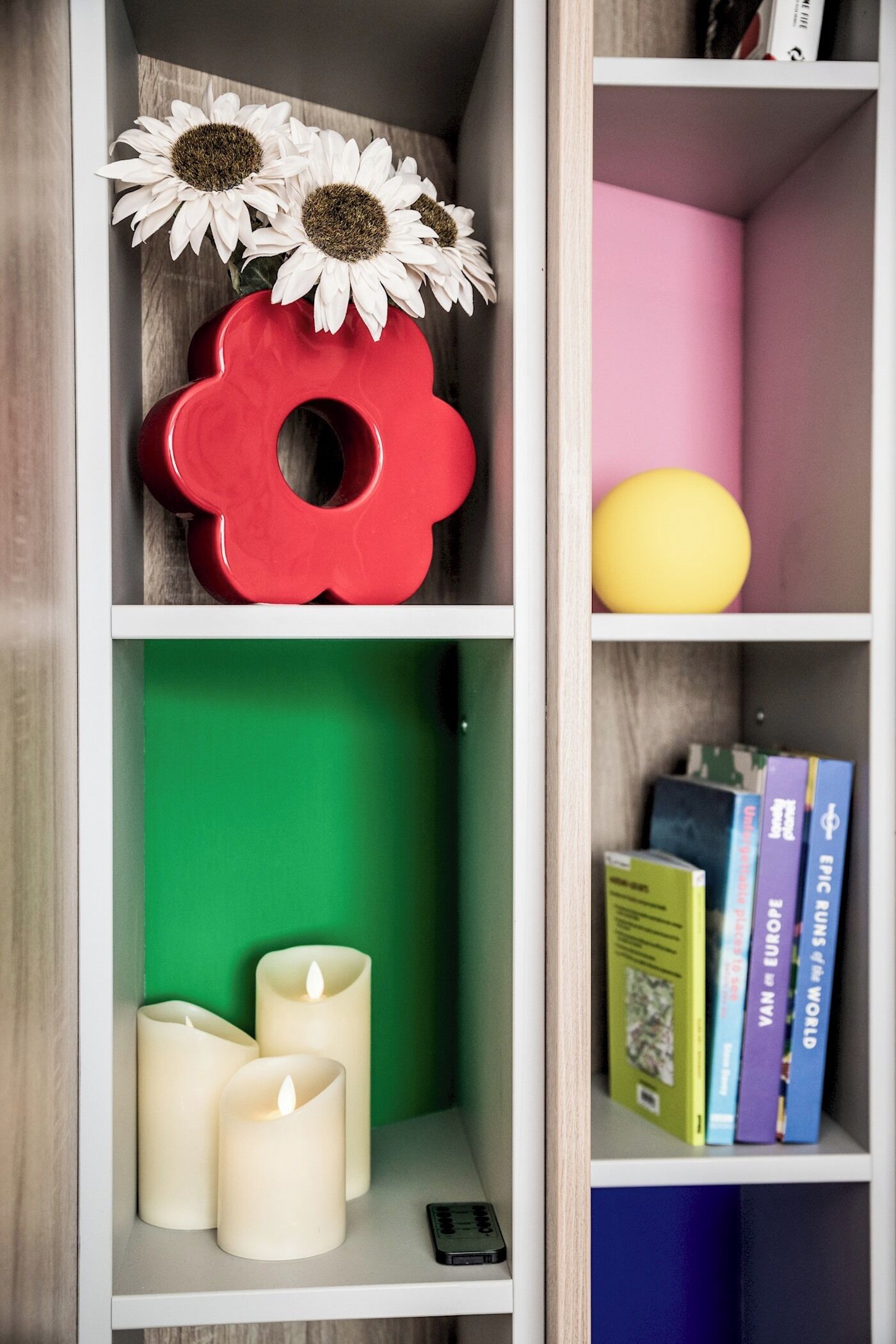 Ein Bücherregal mit Dekorationsobjekten, darunter Sonnenblumen, ein rotes, blumenförmiges Objekt und Bücher.