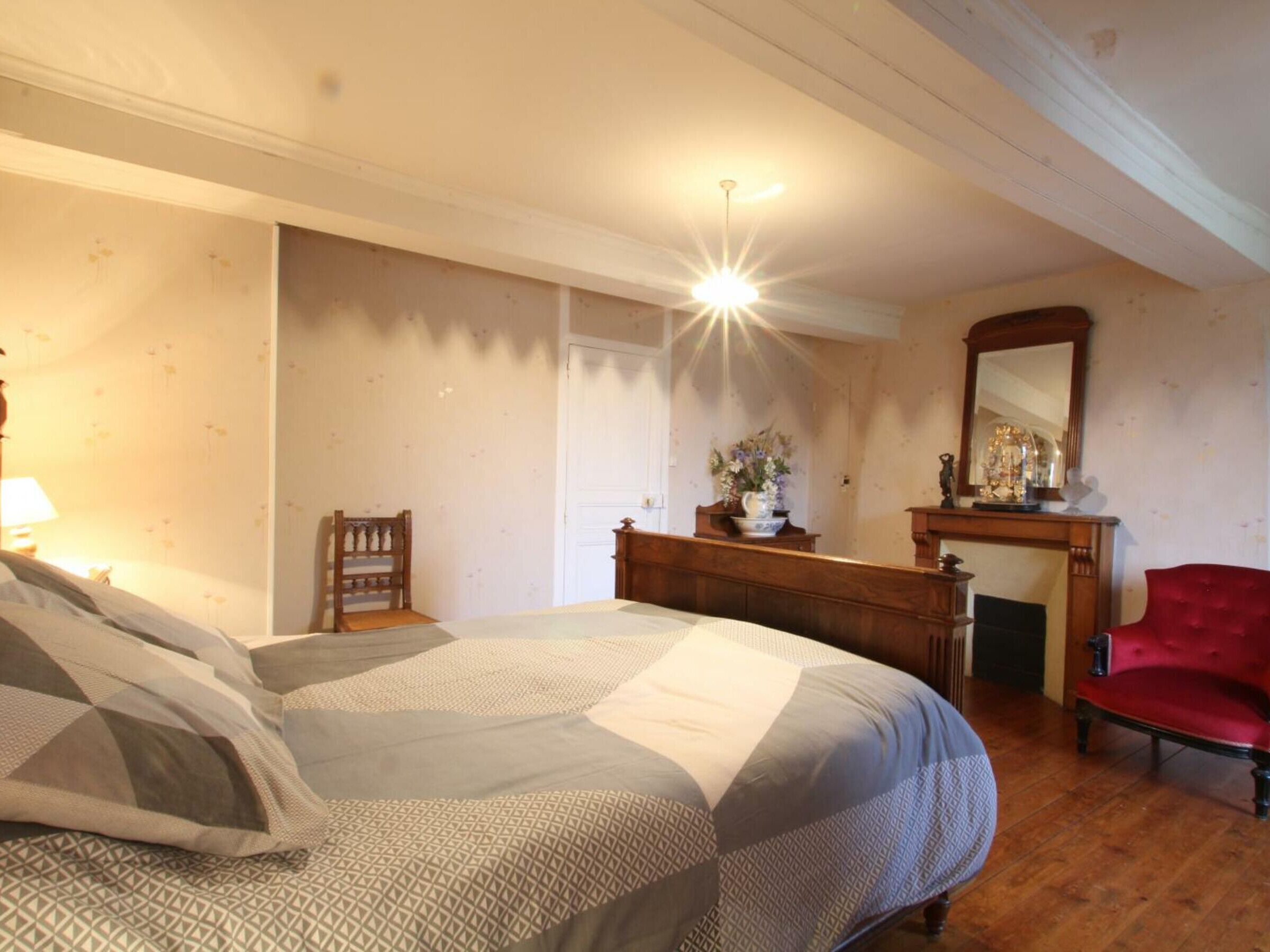Een slaapkamer met een groot bed, een houten dressoir, een rode stoel en een spiegel aan de muur.