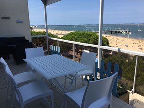 Ein Balkon mit weißem Tisch und Stühlen, mit Blick auf einen Strand mit Booten und einem Steg.