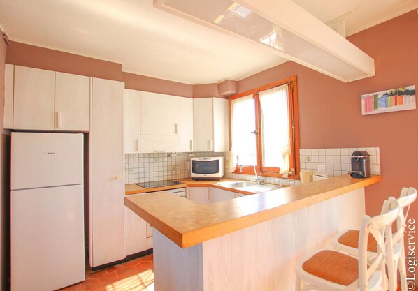 A compact kitchen with white cabinets, a Bosch refrigerator, a microwave, and a wooden island with bar stools.