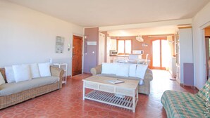 A living room with two wicker sofas, a coffee table, and a kitchen area visible through an open door. - On the beach flat for 4 persons with sea view (PORT-GRIMAUD)