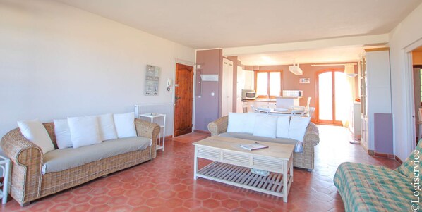 Sala de estar con dos sofás de mimbre, una mesa de centro y una cocina visible a través de una puerta abierta.