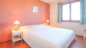 A bedroom with a large bed, two bedside tables with lamps, a window with curtains, and a small picture on the wall. - On the beach flat for 4 persons with sea view (PORT-GRIMAUD)