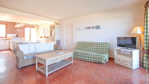 A living room with a sofa, a coffee table, a television on a stand, and a kitchen area in the background. - On the beach flat for 4 persons with sea view (PORT-GRIMAUD)