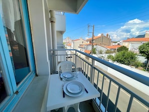 A balcony with a table set for two, a chair, and a view of the neighborhood.