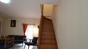 Een trap die naar een verdieping leidt, een eetgedeelte met een tafel en stoelen, en een raam met gordijnen.