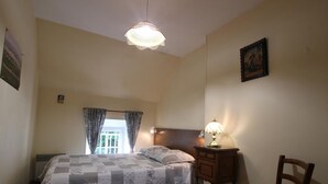 Een slaapkamer met een bed, nachtkastje, stoel, raam met gordijnen en een plafondlamp.