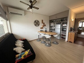 A compact living space with a kitchenette, a dining area with bar stools, and a sofa with cushions.